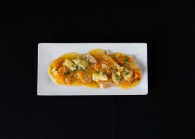 Gourmet fish dish with vegetables on a white rectangular plate.