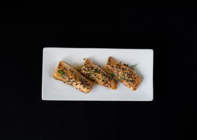 Three toasted sandwiches with herbs on a white plate against black background.