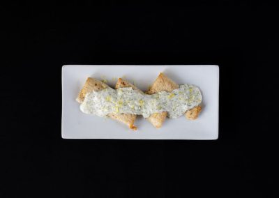 Gourmet dish with sauce on a white rectangular plate against black background.