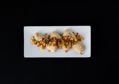Gourmet fish tacos with mango salsa on a white plate against black background.