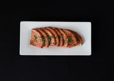 Juicy grilled steak slices garnished with herbs on a white rectangular plate.
