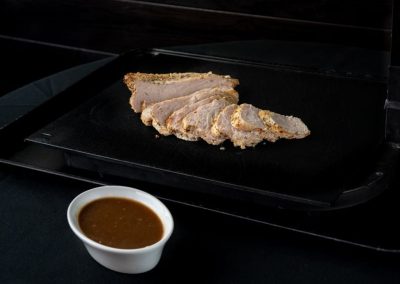 Sliced cooked chicken breast with sauce on black tray.