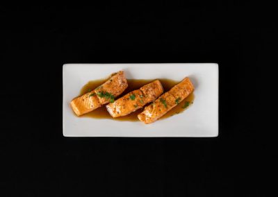 Salmon appetizer with sauce on a white plate against black background.