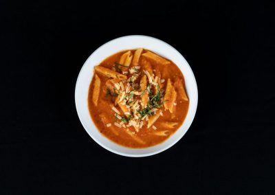 Close-up of spicy pasta with herbs in a white bowl on black background.
