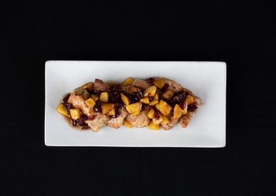Gourmet meat dish topped with fruit and served on a white rectangular plate.