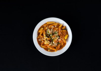 Pasta with tomato sauce, herbs, and cheese in a white bowl on black background.