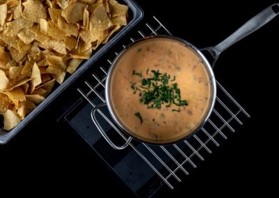 Creamy soup garnished with herbs served with crispy chips on a black background.