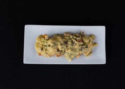 Food dish with creamy topping and herbs on a white rectangular plate.