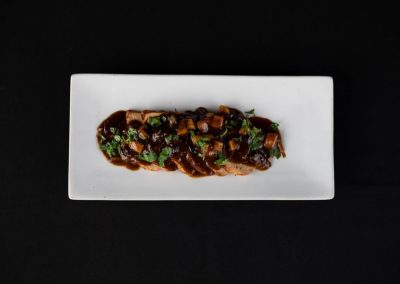 Gourmet beef tenderloin topped with sauce and herbs on a white plate.