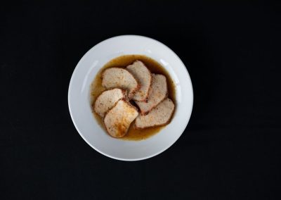 Sliced bread soaking in gravy in a white bowl on black background.