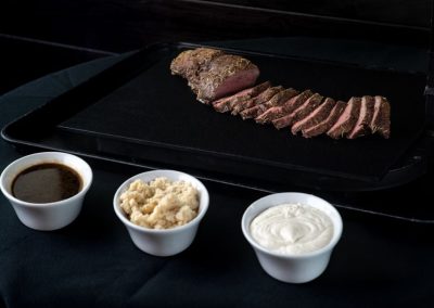 Sous vide steak with three dipping sauces on a black surface.