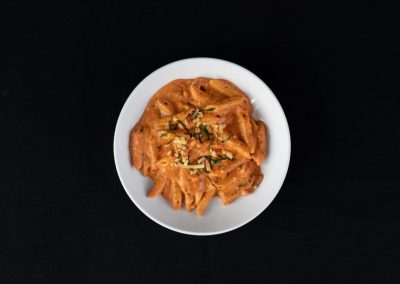 Creamy pasta with herbs served in a white bowl on black background.