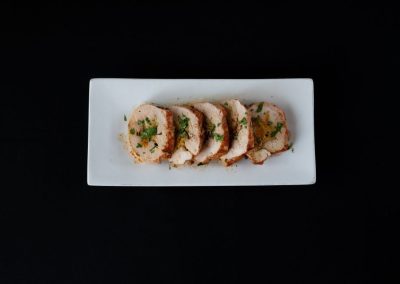 Slices of seasoned chicken on a white rectangular plate against a black background.