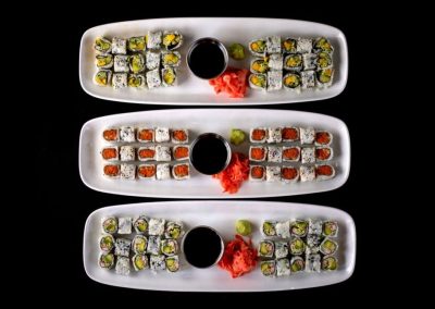 Assorted sushi rolls with soy sauce and wasabi on white plates.