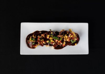 Gourmet dish with sauce, toppings, and herbs on a white plate.