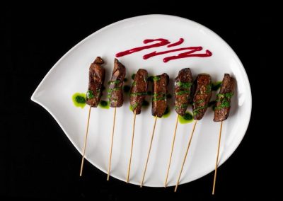 Gourmet beef skewers on a white plate with sauce and herbs.