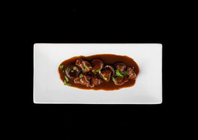 Elegant beef stew with mushrooms and green herbs on a white plate.