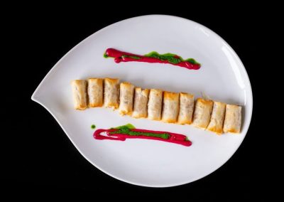 Gourmet sushi roll with colorful sauces on a white plate.