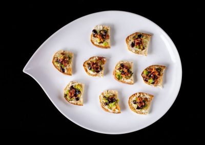 Miniature pizza bites served on a white plate with a black background.