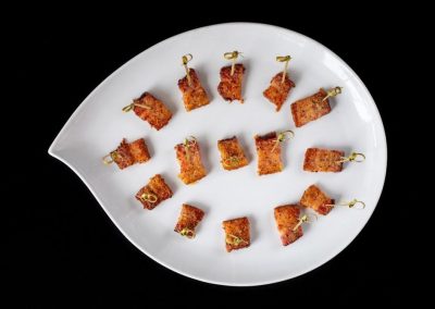 Bacon-wrapped appetizers on a white plate with a black background.