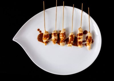 Bacon skewers arranged on a white leaf-shaped plate against a black background.