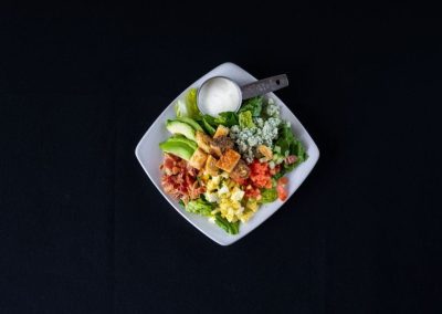 Colorful fresh salad with vegetables and dressing in a white bowl on black background.