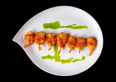 Crispy shrimp skewers with green sauce on white plate.