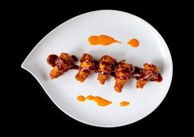 Delicious chicken skewers with sauce on a white plate against black background.