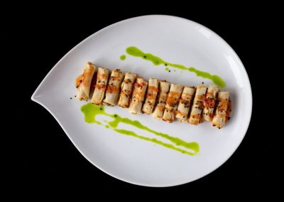 Gourmet sushi roll with green sauce drizzle on white plate.