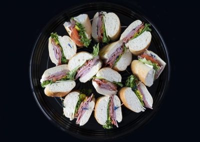 Variety of sandwiches with meats, cheese, and vegetables on a black plate.