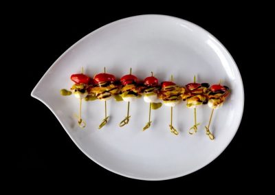 Skewers with cherry tomatoes, cheese, and meat on a white plate.