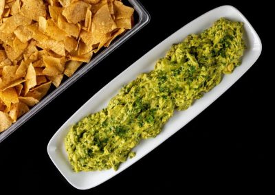 Guacamole with tortilla chips on a white platter for snacking.