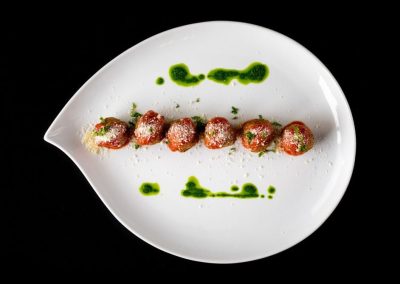 Gourmet meatballs with green sauce on a white plate.