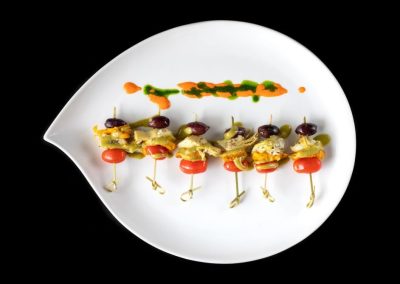 Gourmet vegetable and olive skewers on a white plate with sauce.