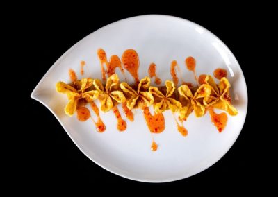 Elegant food presentation with fried items and orange sauce on a white leaf-shaped plate.