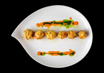 Crispy fried appetizer with colorful sauces on a white plate.