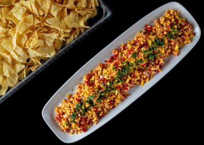 Vibrant corn salsa with herbs on a white dish, black background.