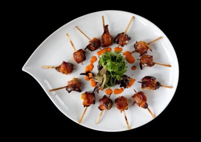Bacon-wrapped appetizers arranged on a white plate with garnish.