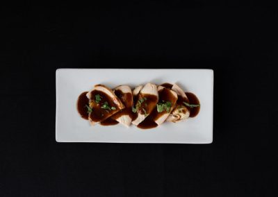 Gourmet chicken dish with sauce and herbs on a white plate.