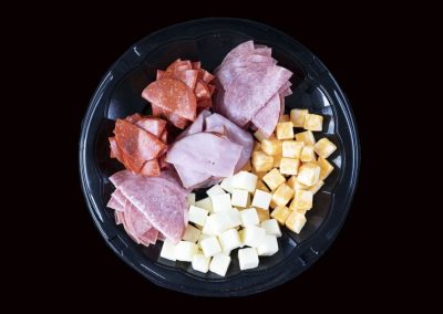 Variety of sliced meats and cheeses on a black plate for appetizer.
