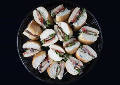 Variety of small sandwiches on a black platter for catering or events.