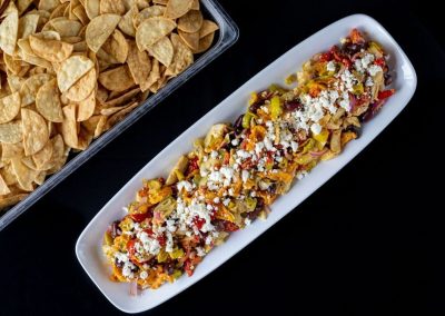 Colorful loaded nachos with cheese, vegetables, and toppings on a white platter.