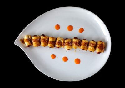 Gourmet sushi roll with sauce dots on a white plate against black background.