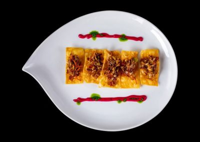 Delicious ravioli with meat topping on a white plate with sauce decoration.