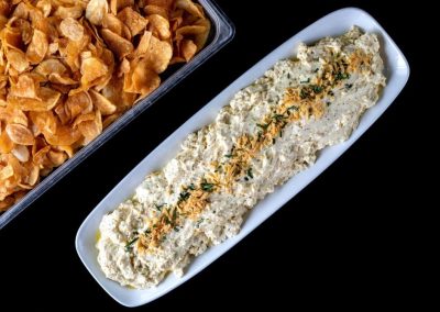 Creamy dip garnished with herbs on a white platter with crispy chips nearby.