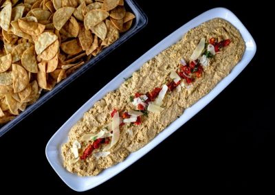 Appetizer platter with hummus, red peppers, and pita chips.