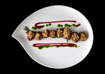 Fried food skewer with garnishes and sauces on a white plate.