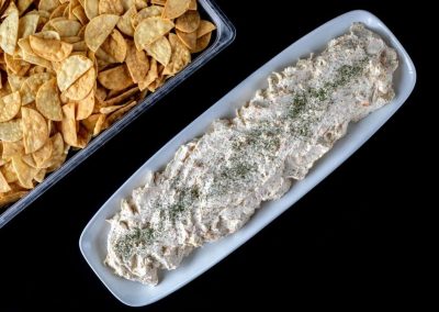 Creamy dip with herbs served on a white dish with chips nearby.