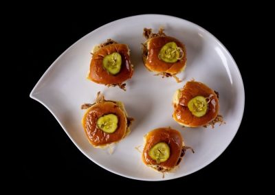 Indian sweets with green garnish on a white plate against black background.