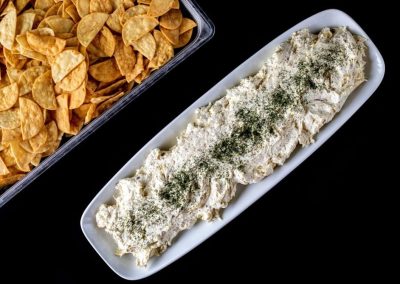 Food platter with seasoned chicken and potato chips on black background.